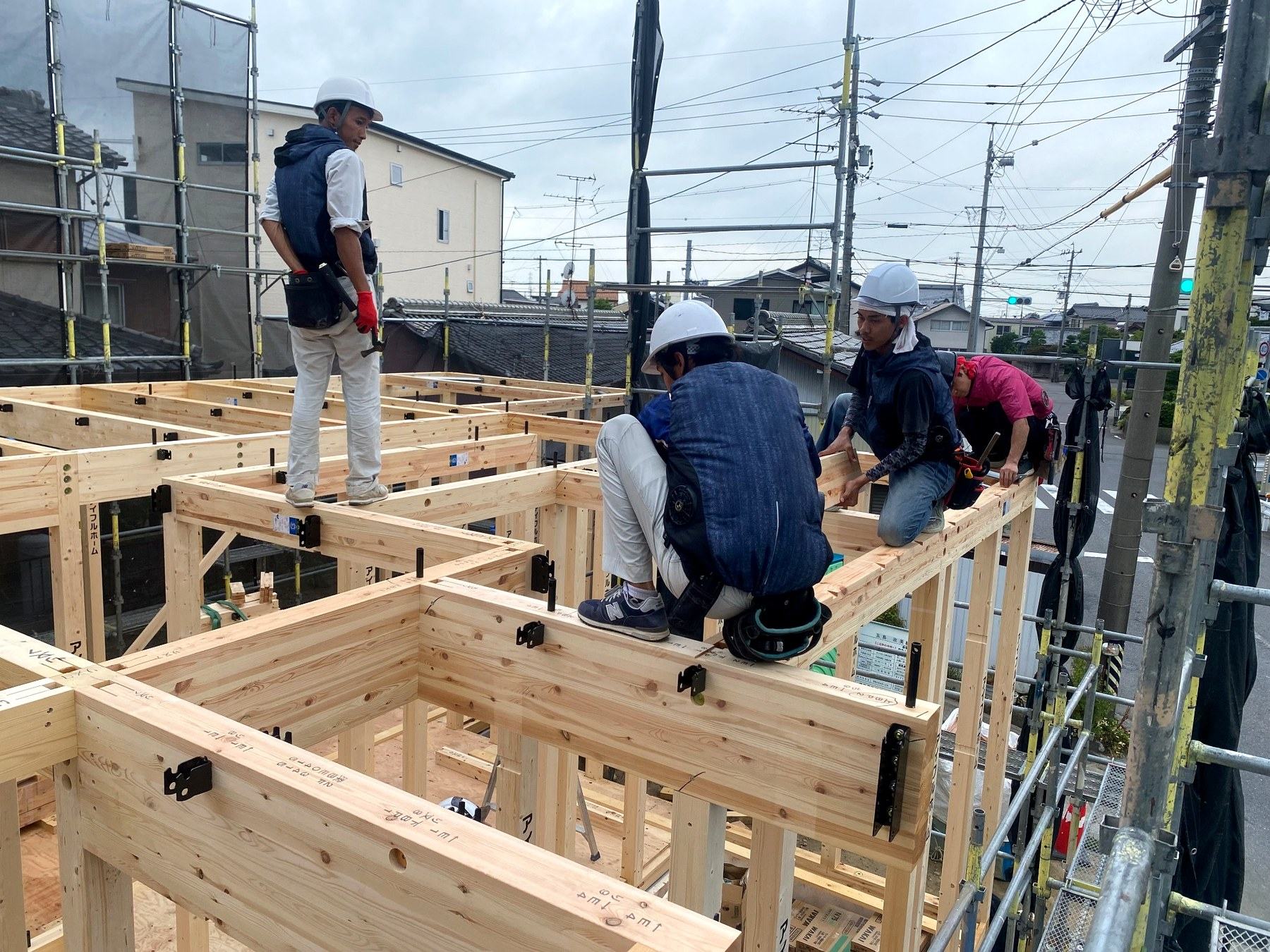 木造住宅の梁の上で連携して作業する職人たち